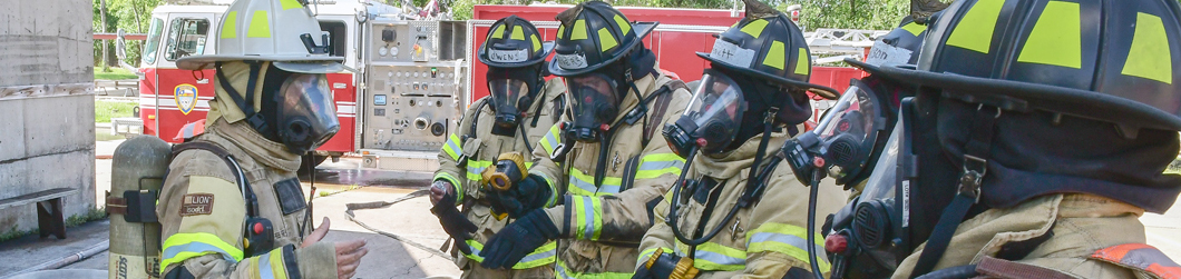 firefighters in gear gathered around having a discussion at training academy
